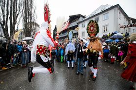 Kostümierter Maskenmensch hüpft auf Fasnacht, viele Menschen im Hintergrund